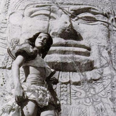 Burnu Acquanetta posing in a Mexican costume in front of a fake Olmec head