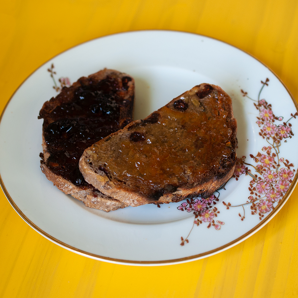 a slice of toast with orange marmalade, on top of a slice of toast with huckleberry preserves